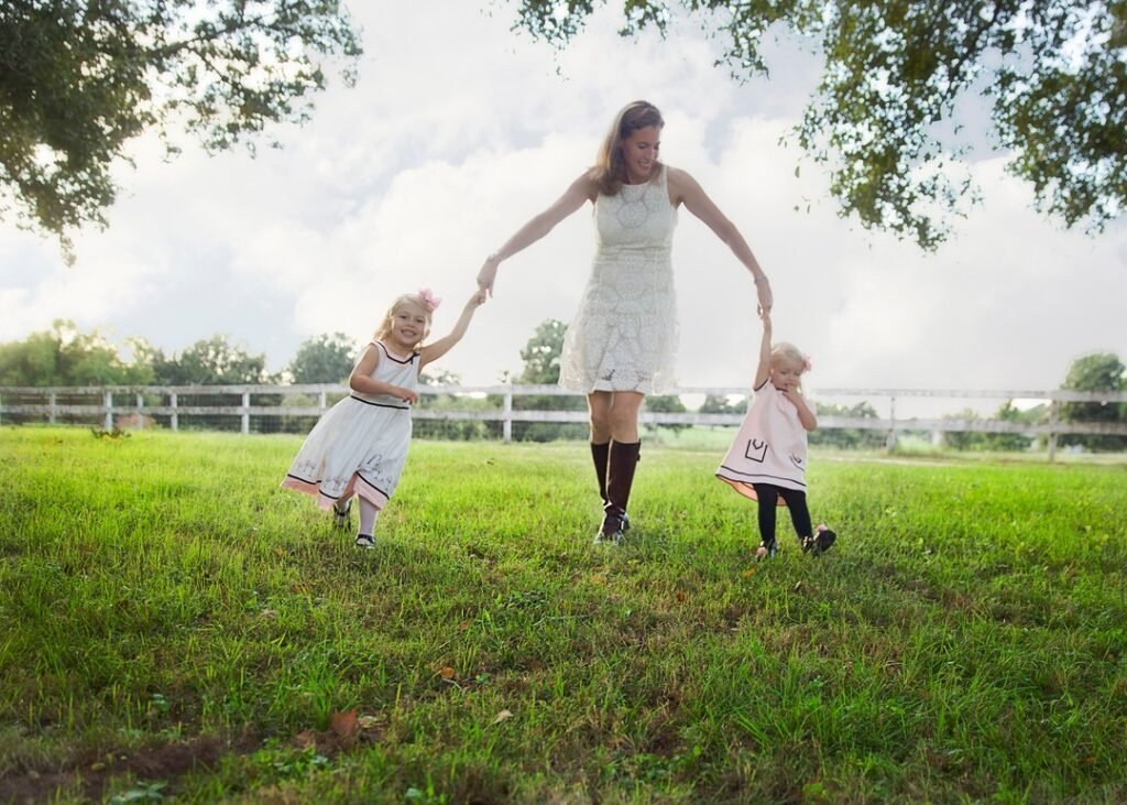 Two little girls spin while holding on to their mother's finger in a field during and epic session.