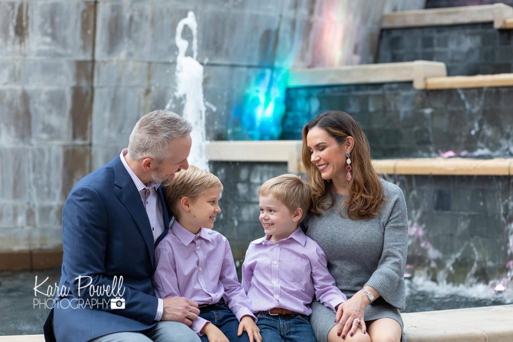 Woodlands Waterway Photographer - Family of 4 sits in front of a water fountain