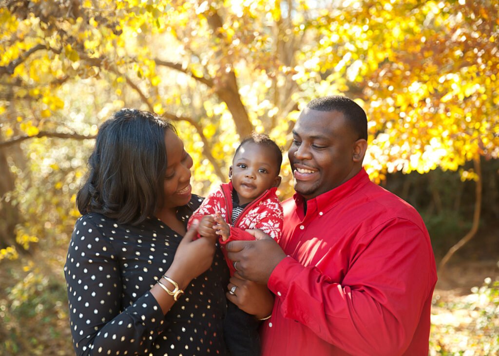 Happy couple holding child in fall season in the woodlands texas for a family photo session