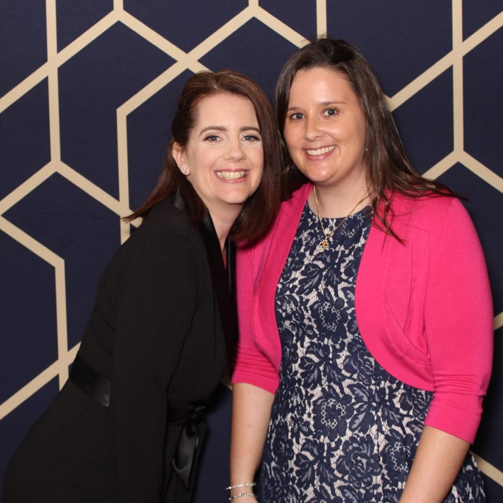 Teamwork is dreamwork for the two photographers pictured in this photo. A Navy blue and gold background is behind the photographers.