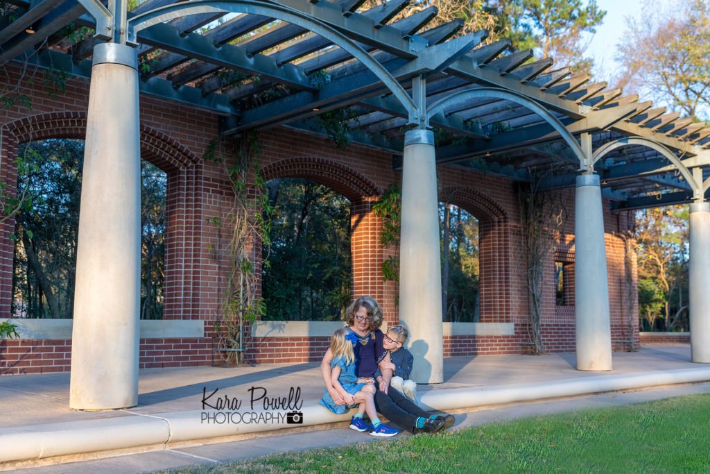 A grandmother and her two grandchildren sitting in front of a brick wall photographed by a grandparent photographer.