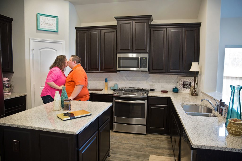 A couple kisses in the kitchen of their new home: one of the reasons why are photography sessions best at home