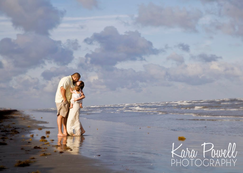A couple stands on the beach holding their daughter, kissing. This is why you should print photos.