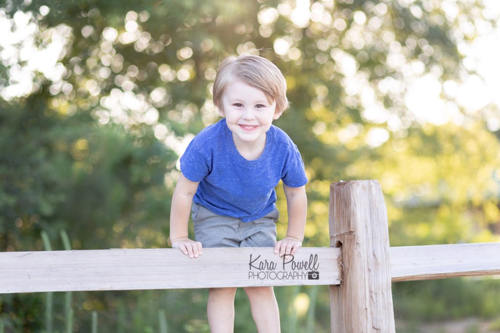 A young boy plays on a fence while posing for his three year old birthday session.