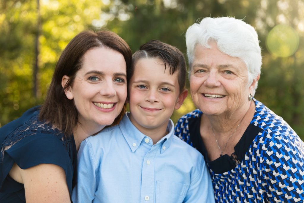 A grandma, mom and son pose together in the trees for a Mother's Day photo session.