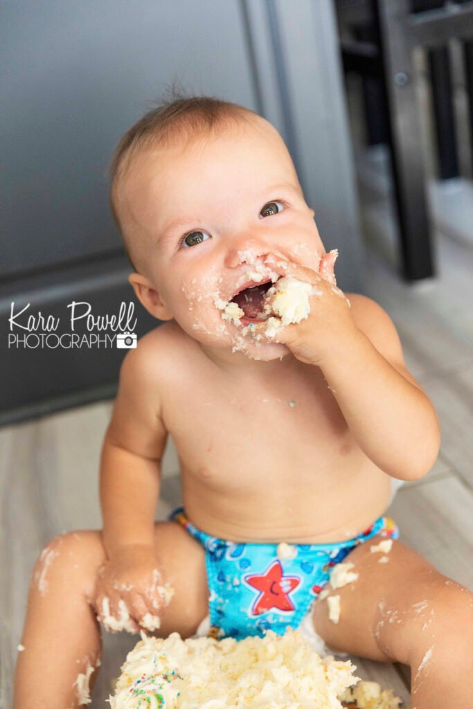 One year old boy doing a cake smash session with a messy cake covered face.