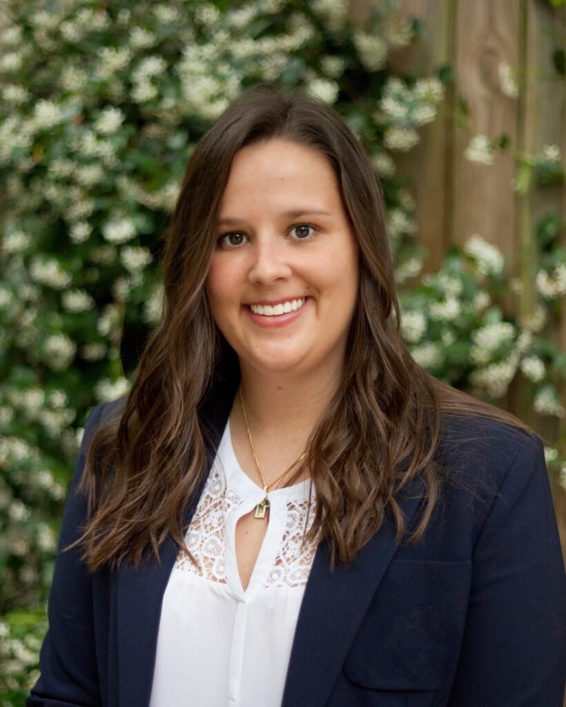 Headshot photo of a woman who does photo editing in front of a flower and vine covered fence