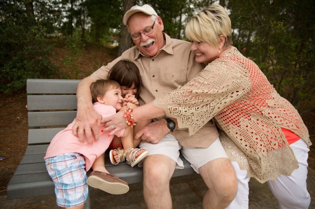 A grandmother and grandfather snuggle with their grandkids on a park bench. Grandkids love portraits of grandparents