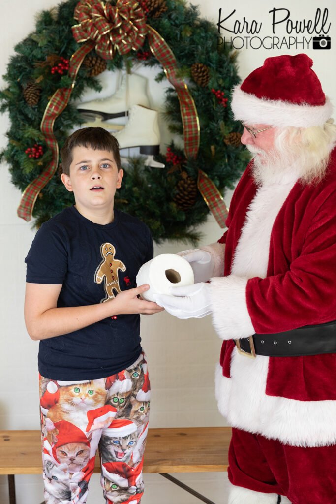 Little boy who looks shocked to be receiving a roll of toilet paper from Santa at his Santa Session.
