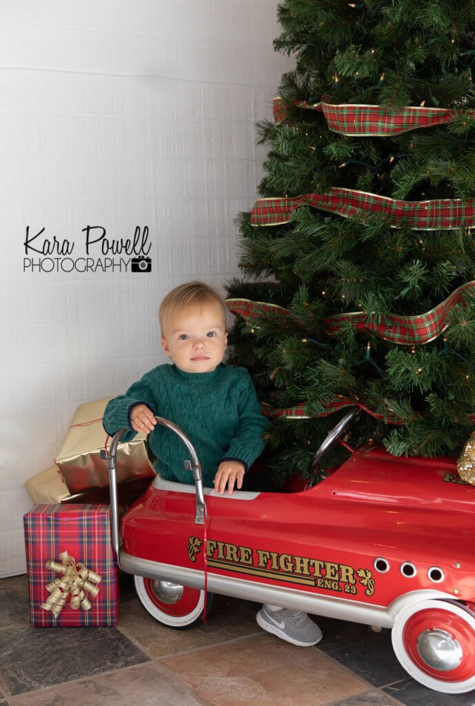 A little boy sits in a toy car under the Christmas tree at his Quiet Time with Santa Session.