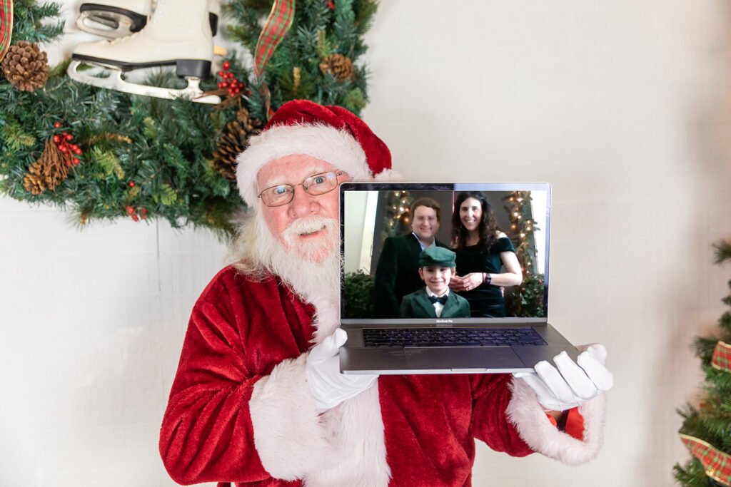 Santa holds up his computer where he is doing a zoom meeting with one of his favorite kids in Canada at Kara Powell Photography's Santa Photo Sessions
