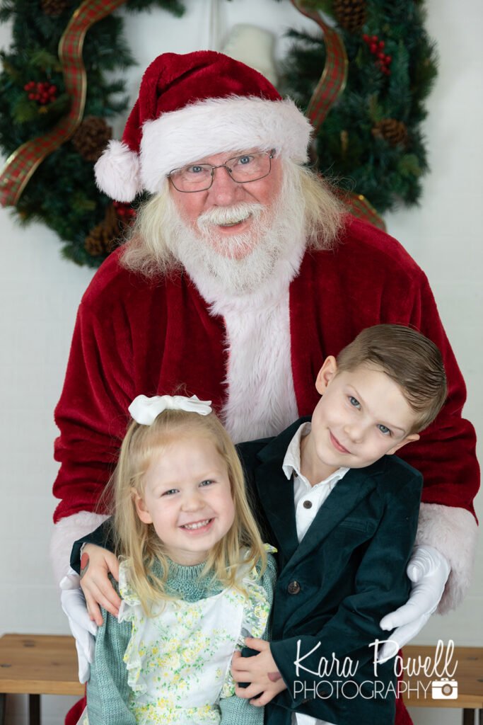 A brother and sister smile with Santa Claus