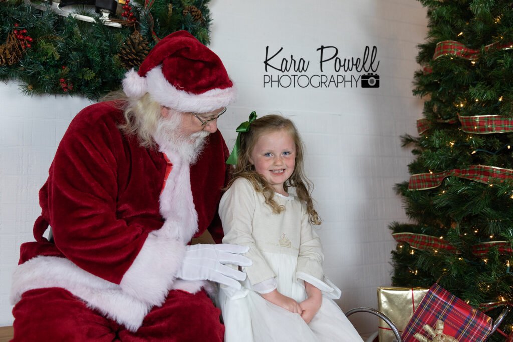 A shy little girl smiles with Santa Claus at her Quiet Time With Santa Session.