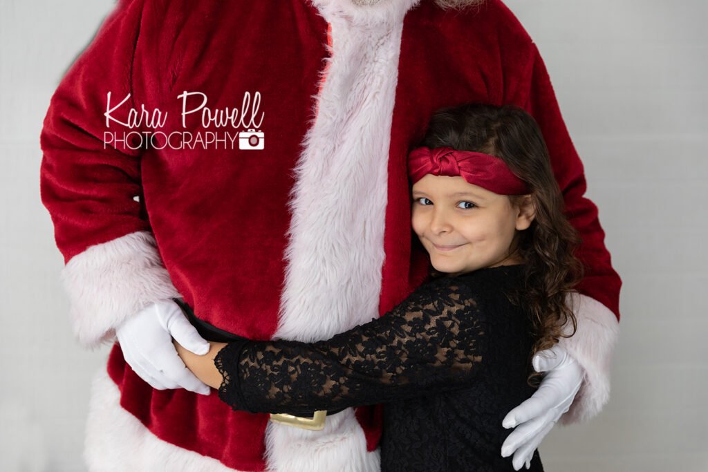 A little girl hugs the waist of Santa Claus