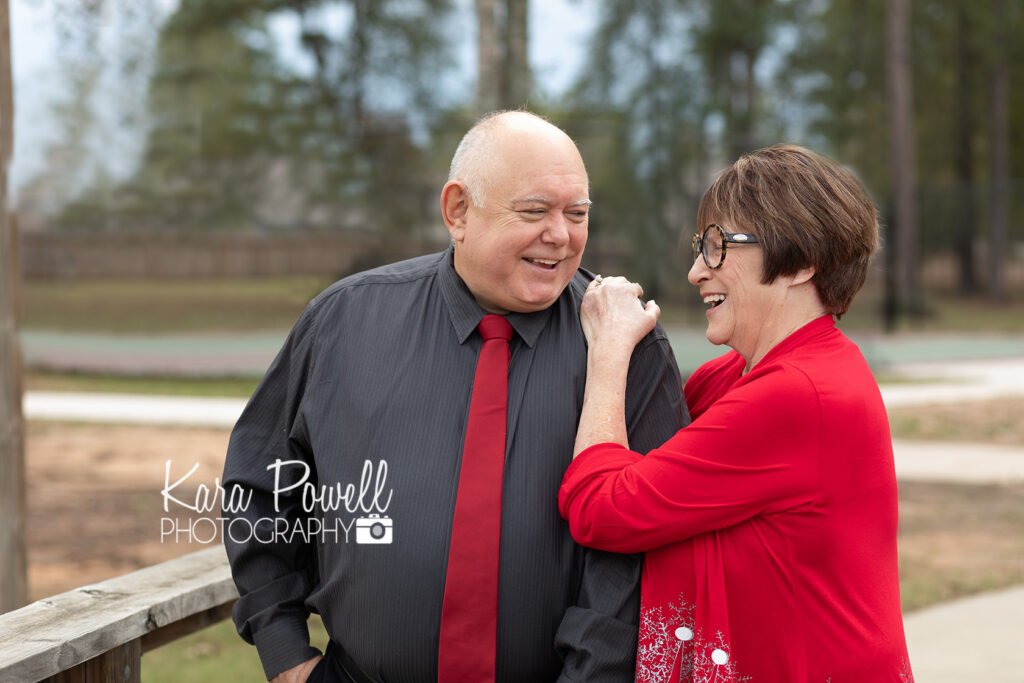 An older couple laugh together in a park while having couples photos taken.