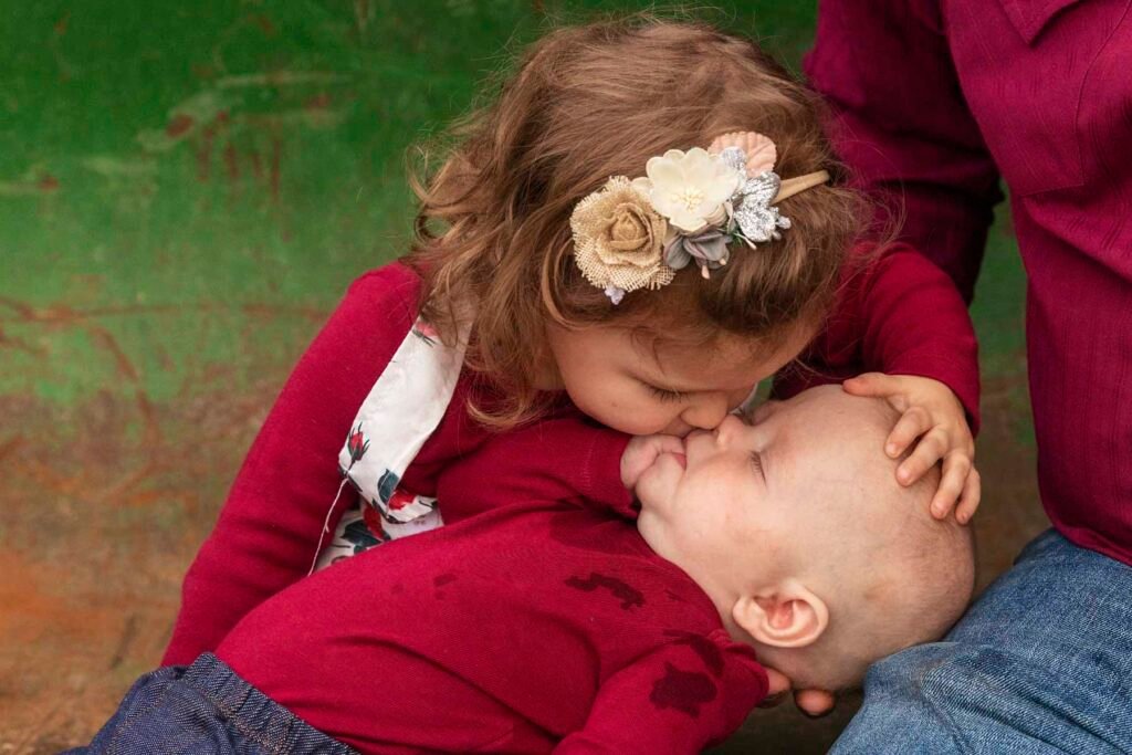 A little girl kisses her brothers nose