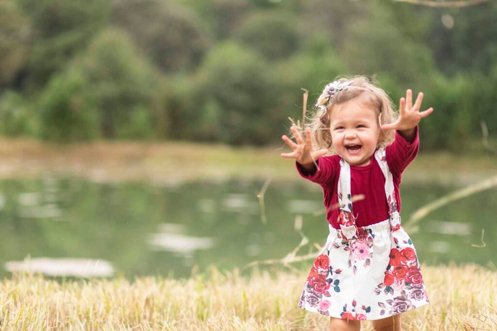 A little girl in the Tippy Toes Baby Plan throws grass while giggling.
