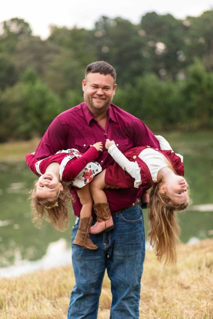 A dad holds his two daughters and smiles for their tippy toes baby plan
