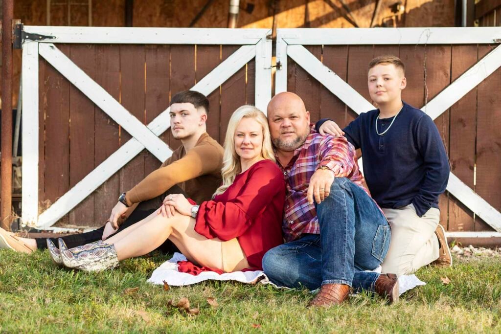Family of four poses in front of barn doors at Townhall TX