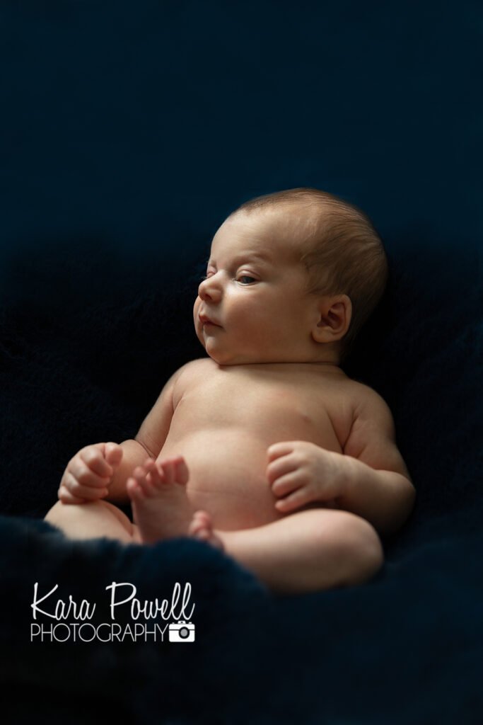 A newborn baby on a blue background during his awake newborn session
