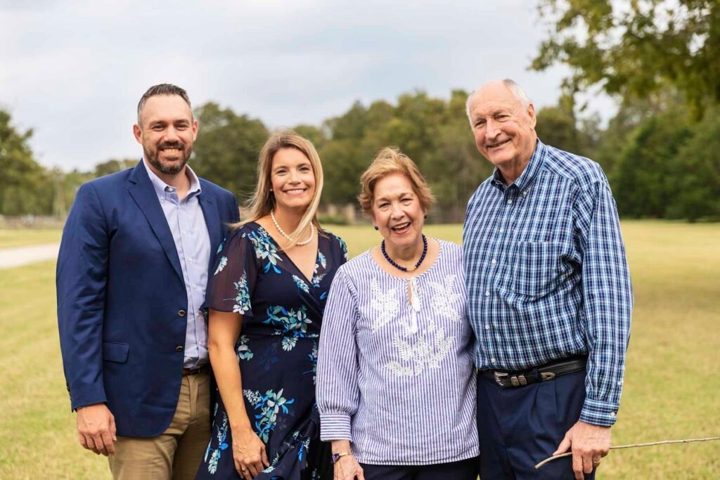 Four adults stand together in a field smiling.