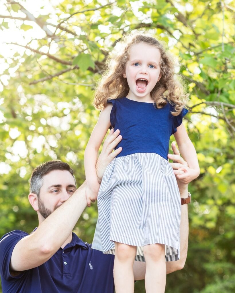 A little girl is held in the air by her dad as she is photographed by a childrens photographer.