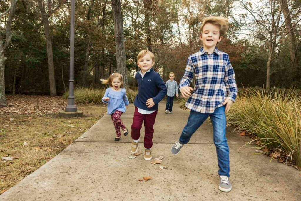 Cousins running through a park during fall in Tomball TX